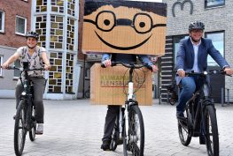 3 Personen auf Fahrrad. Mittig Kalle der Karton in Menschengestalt