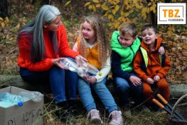 4 Personen im Rahmen der TBZ-Rallye beim Müllsammeln / untersuchen im Wald. Im hintergrund das TBZ Logo.